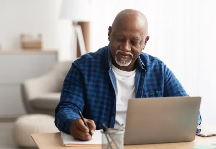 An older bald man with a silver goatee writes a note to himself